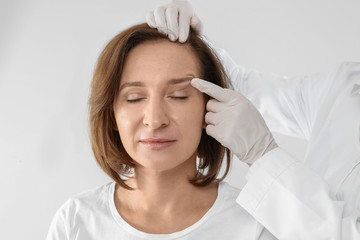 Doctor examining mature woman face before cosmetic surgery on white background