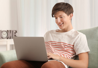 Cute teenager boy using laptop while doing homework indoors