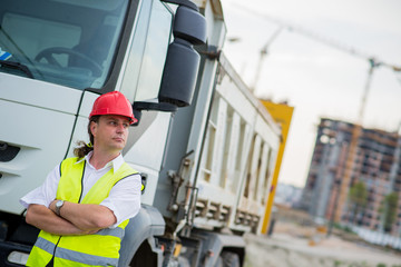 Truck driver in front of a truck on a construction site with his arms crossed