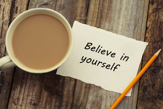 Believe in yourself inscription on white papper. Cup of cofee and pencil over rustic wooden background.