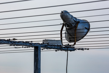 Obraz premium External single cone tin floodlight on metallic steel t-shaped stand with multiple metallic strings, crossing the image, some of them blurred and out of focus