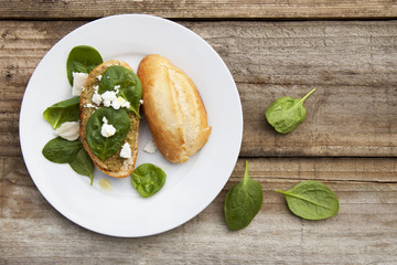Healthy snack. Bun or bread with pesto pasta and basil leaves. Rustic wooden table, top view.