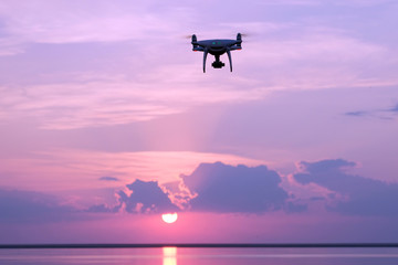 Silhouette of a drone at sunrise over the lake against the sky with the rising sun. Quadcopter, clouds, morning sunlight. Aerial photo and video. Copy space.