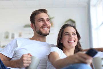 Fototapeta premium Young loving couple on sofa at home watching tv and laughing.