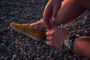 Close-up arms and leg of a man sitting on a pebble beach at sunset. Outdoor recreation. Lifestyle concept.