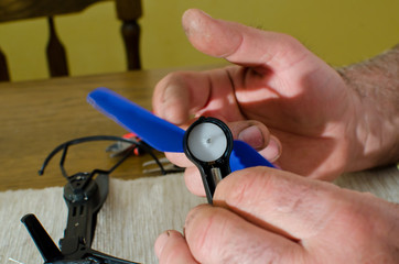 hands of man repairing small black drone with blue propeller  