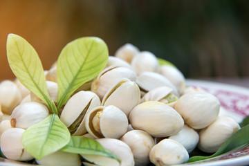 Close up of Pistachios nuts on wooden table. Pistachio in wooden bowl in background with green leaves