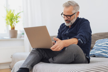 älterer mann sitzt auf der couch und arbeitet am laptop