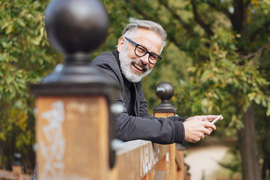 mann lehnt drau&szlig;en auf einem holzgel&auml;nder und h&auml;lt sein handy in der hand