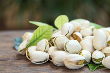 Close up of Pistachios nuts on wooden table. Pistachio in wooden bowl in background with green leaves