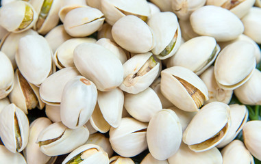 Close up of Pistachios nuts on wooden table. Pistachio in wooden bowl in background with green leaves