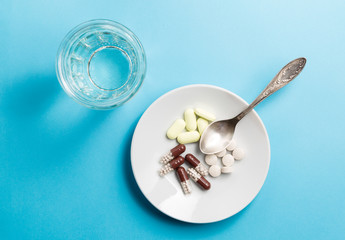 A spoon with a pile of medicines and a glass of water.