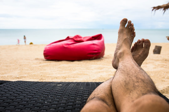 Feet On Beachchair At Beachfront With Red Beanbag Background