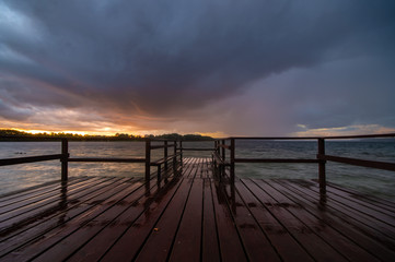 Fototapeta na wymiar evening storm over the lake, the sky reflecting off the wet planks of the wooden jetty
