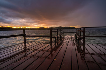 Fototapeta na wymiar evening storm over the lake, the sky reflecting off the wet planks of the wooden jetty