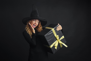 Black Friday. Halloween witch with a black hat on a black background holding gift boxes with juruse in her hands. Surprise and gift on sale