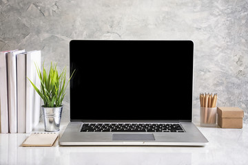 Mockup laptop computer laptop with office supplies on white table with concrete wall