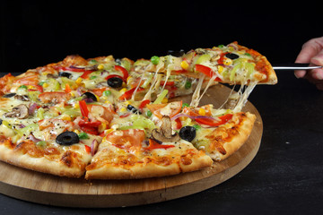 Vegetarian multicolored pizza, cut into pieces, one of which is pulled with a spatula
