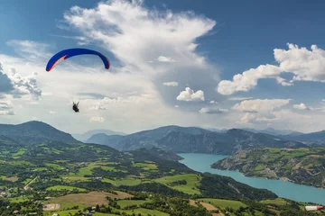 Tuinposter Bright paraglider tandem wing fly over beautiful mountain valley with green hills and blue lake. © Mny-Jhee