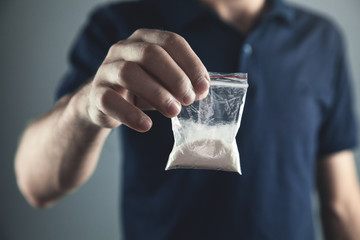 Drug dealer holding plastic packet with cocaine powder.
