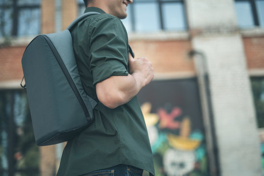 Convenient backpack. Young man wearing casual clothes and feeling glad while standing with convenient grey backpack