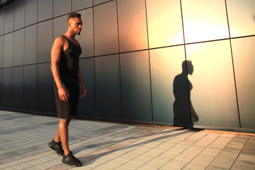 Obraz na płótnie Canvas Full length of young African man in sports clothing jogging while exercising outdoors, at sunset or sunrise. Runner.