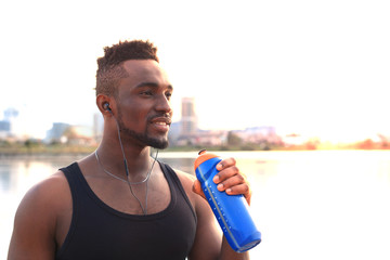 African man in sports clothing drinking water exercise in beach outdoor portrait, at sunset or sunrise.