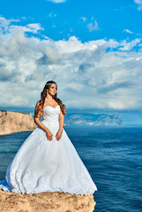 Fototapeta na wymiar Brunette bride in a long white dress near the sea