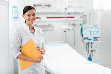 Waist up portrait of female medical worker holding orange envelope while looking at camera with...
