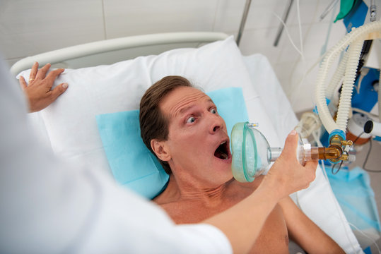 I am terrified. Close up of middle aged man with oxygen mask lying in bed with wide opened eyes and mouth