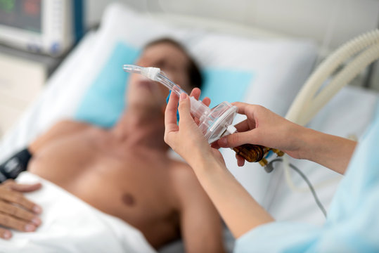 Mechanical ventilation. Close up of female hands preparing tube of breathing machine while middle aged man lying in hospital bed