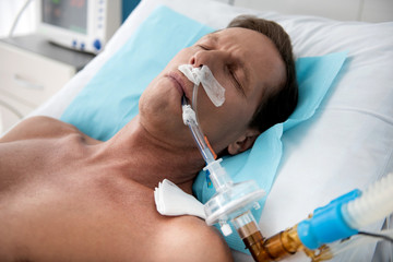 Close up portrait of middle aged man on breathing machine sleeping in hospital bed after surgery