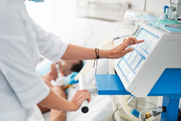 Close up of female hands checking medical equipment. Patient on breathing machine lying in bed on...