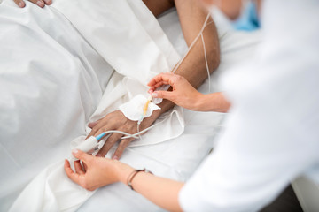 Close up of female hand touching intravenous drip and pulse oximeter sensor on man arm. Gentleman...