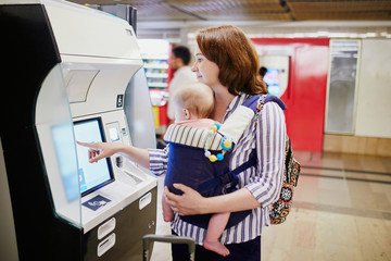 Woman with little kid in baby carrier doing self check in at airport