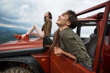 Cheerful beautiful young woman enjoying her active weekend with her friend while traveling in the off-road car