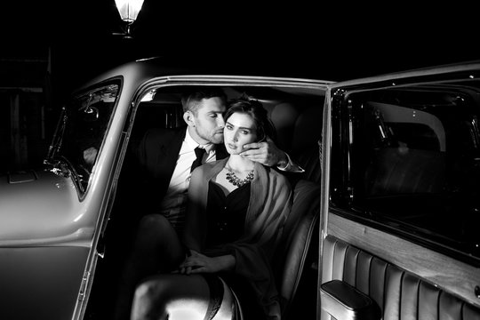 Good looking sexy couple, handsome man in suit, beautiful woman in red dress, embrace passionately in vintage car