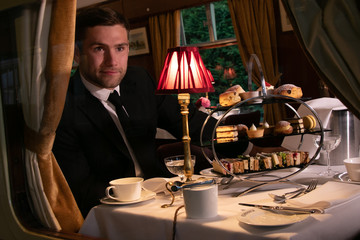 Good looking man in suit enjoying afternoon tea in vintage train carriage