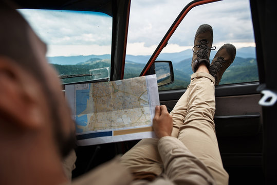 Adventurous male expeditor sitting in the car while exploring map of the Carpathian mountains