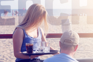 The waitress is carrying drink to the client of in a cafe on the beach. Waitress serving a client...
