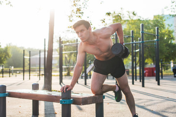 Muscular male athlete with arms raised doing lifting exercises dumbbells.