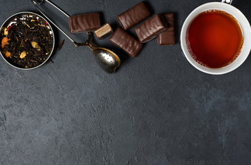 Chocolates and black tea with herbs. Metal tea strainer. Dark background. Copy space. Flat lay
