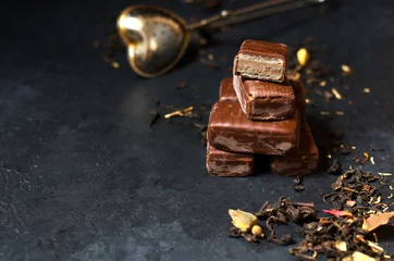 Rolgordijnen Chocolate candy and black tea with herbs. Metal tea strainer. Dark background. Copy space © mitand73