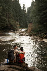 Peaceful stream. Kind loving man gently hugging his beloved woman while sitting near the river with her