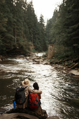 Beautiful water. Beautiful young couple of travelers hugging while sitting on the stone and looking at the water stream