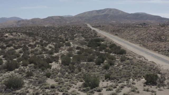 Aerial fly over of a road in a barren desert land with some small shrubs.