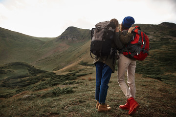 Friendship and mountains. Active young hikers standing close to each other and wearing backpacks while traveling in the mountains