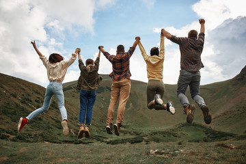 Jumping high. Expressive young group of friends feeling excited and jumping while being on the top...