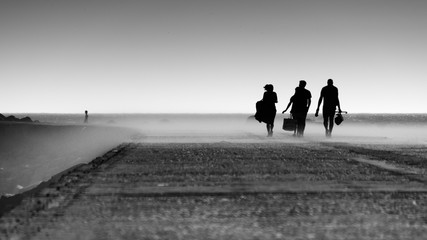 Silhouette of fishermen returning from their fishing spot in a concrete sea pier on a windy late afternoon in a sand cloud, Black and White Photo, Figueira da Foz, Portugal.
