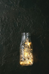 Christmas lights garland in glass bottle over dark texture background. Christmas holiday mood card. Top view with space